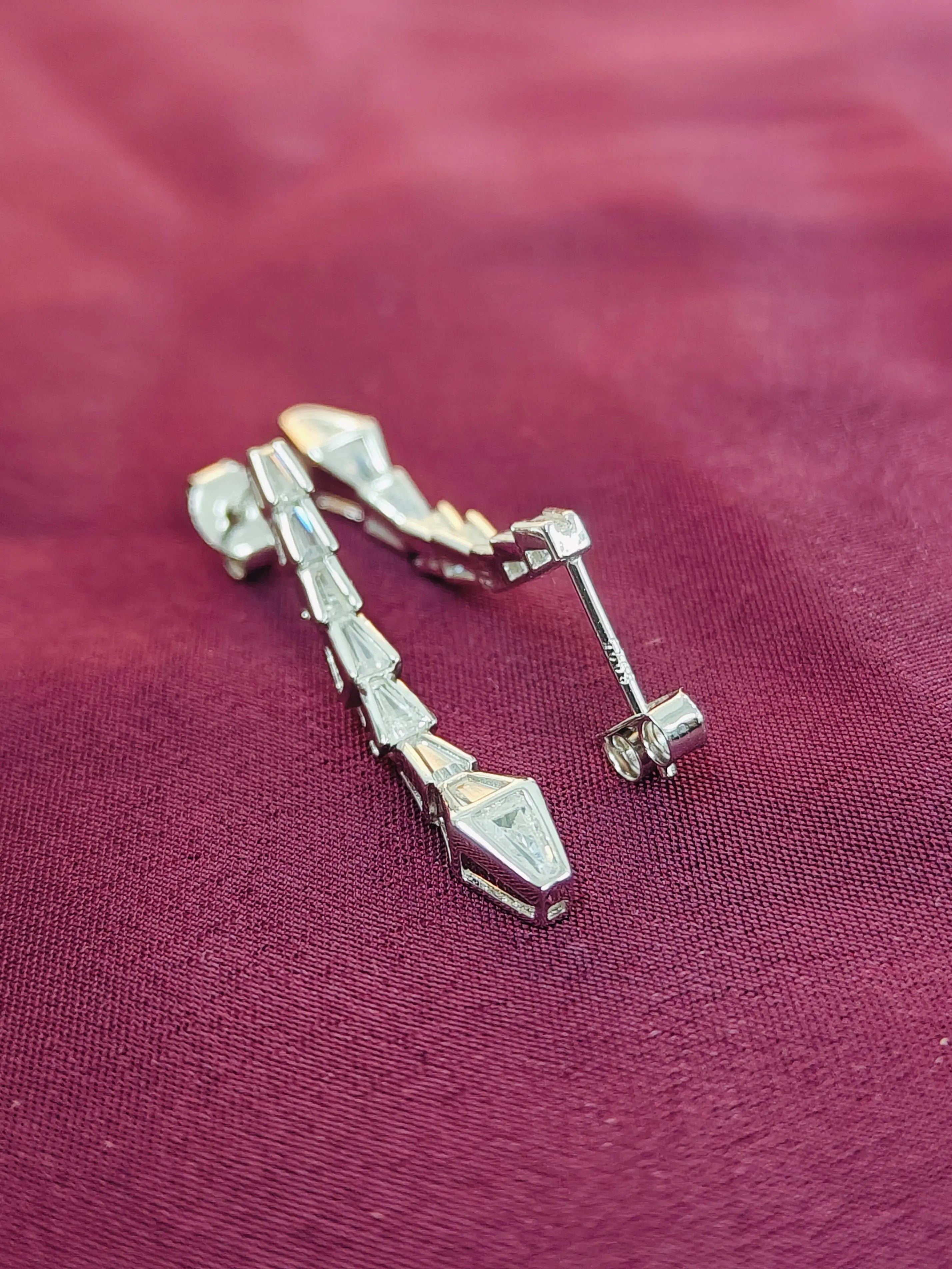 Silver earring on a maroon fabric background